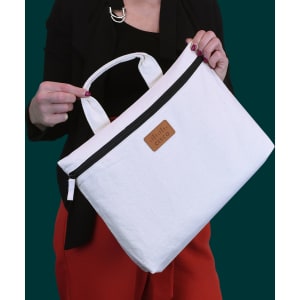 A white conference bag with a black zipper, featuring a logo, held by a person against a dark green background.
