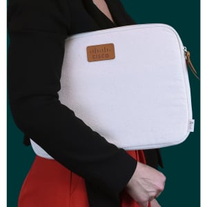 A cream laptop sleeve with a leather tag, being held by a person in a black jacket.