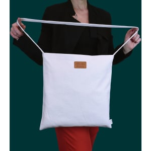 A white tote bag with a long handle, featuring a logo on the front, held by a person wearing a black top.