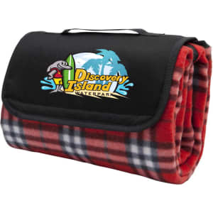 A red check picnic rug folded with a black carrying strap and featuring a logo on the front.