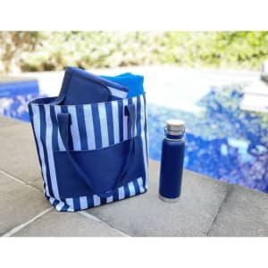 A navy and white striped tote bag with a drink bottle and additional items inside, placed beside a pool.