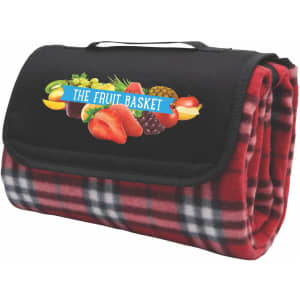 A folded red check picnic rug featuring a black canvas flap with a logo, showcasing a fruit graphic.