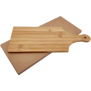 A bamboo cheese board with a handle, placed on a brown cardboard backing. It features a natural wood finish.