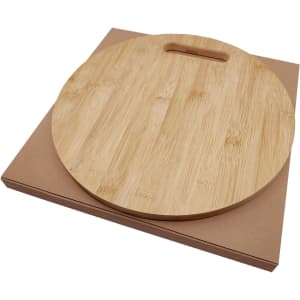A round bamboo cheese board with a handle, resting on a brown kraft box.