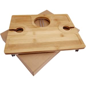 A bamboo picnic board with cutouts for glasses and a central hole, placed on a kraft paper box.