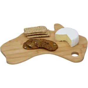 A bamboo cheese board in the shape of Australia with cheese, crackers, and cookies displayed on top.