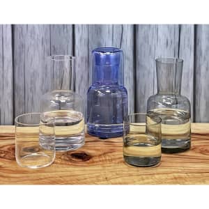 A glassware set featuring a blue carafe and four tumblers in clear and tinted glass on a wooden surface.