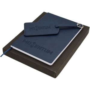 A navy travel journal set with a notebook and a matching luggage tag, presented in a dark box.