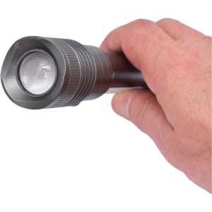 A gunmetal torch with a textured grip held in a person's hand, featuring a round lens at the front.