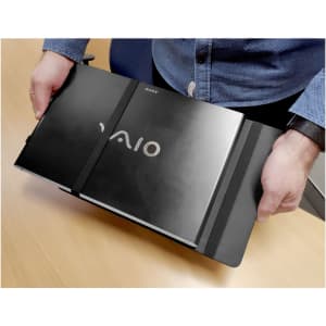 A person holding a black laptop bag with an elastic strap, containing a silver Sony Vaio laptop.