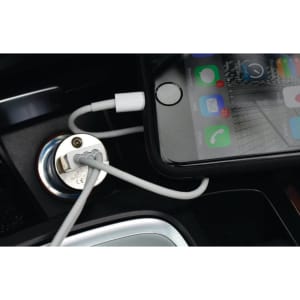 A phone charging cable connected to a silver car charger, with a smartphone displaying apps and notifications.