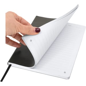 A hand holding an A5 notebook with a black cover, showing blank lined pages inside. The notebook has a ribbon bookmark.