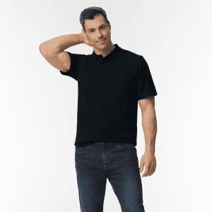 A man in a black polo shirt poses with one hand on his neck, wearing blue jeans. The shirt features a logo.