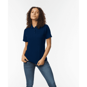 A model wearing a navy blue ladies' double pique polo shirt, featuring a logo, paired with denim jeans.