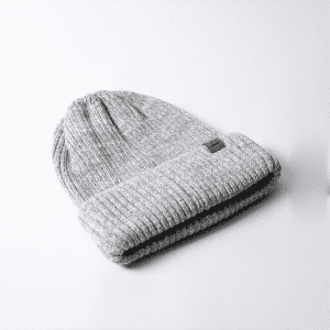 A grey beanie with a rolled cuff, featuring a small logo. It's made from a textured knit material.
