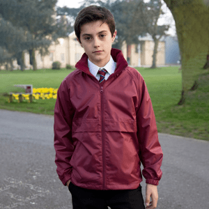 A youth wearing a maroon jacket stands outdoors, surrounded by greenery. The jacket features a logo on the front.