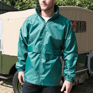 A man wearing a teal rain jacket with a high collar, standing outdoors near a vehicle. The jacket has a logo.