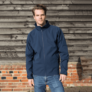 A navy softshell jacket with a high collar, featuring a front zipper and an unseen logo, worn by a model.