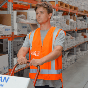 An orange high-visibility safety vest with reflective strips, worn by a person in a warehouse setting.