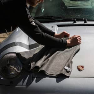 A grey car drying towel is being used on a silver car bonnet, with a logo visible on the vehicle.