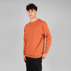 An orange crewneck jumper displayed on a model against a neutral background. The jumper features a subtle logo.