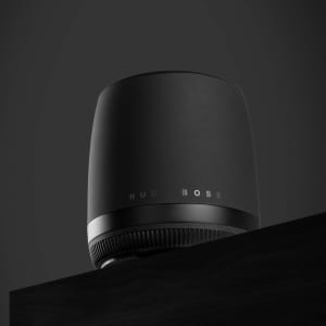 A sleek black Hugo Boss speaker with a rounded design sits on a dark surface. It features a subtle logo.