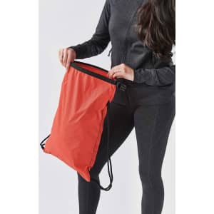 A red drawstring bag is being held by a person wearing dark athletic clothing. The bag has a black drawing cord.