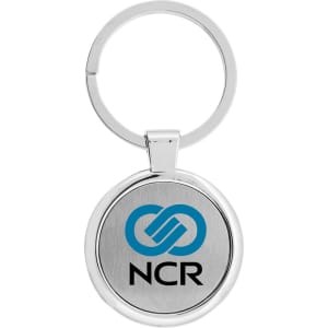 A silver keychain featuring a circular design with a branding logo on a metal surface.