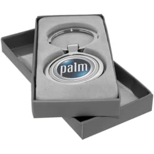 A silver keychain with a circular emblem in a grey box with a soft interior. The keychain includes a logo.