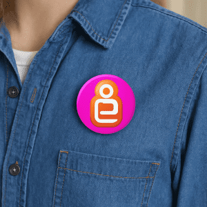 A 32mm button badge in pink with a circular design, displayed on a denim shirt pocket.