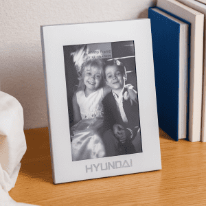 A silver aluminium photo frame displaying a black-and-white photo of two children. The frame features a logo at the bottom.