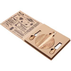 A round wooden cheeseboard with two cheese knives, displayed in a cardboard presentation case featuring various designs.