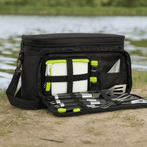 A black picnic bag with green accents, containing cutlery, a chopping board, drink bottles, and various food prep tools.