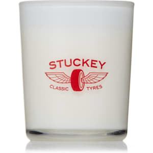 A glass candle with a white wax interior and a red logo featuring wings and a tyre motif.