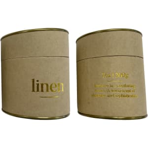 A large candle in a cylindrical kraft paper container with gold accents, labelled 'linen'.