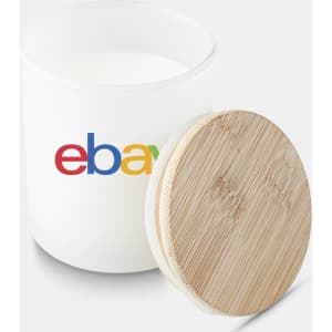 A large white candle in a glass jar with a bamboo lid and a logo on the side.