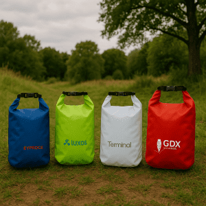 Four dry bags in blue, green, white, and red, featuring logos on each bag, set in a grassy outdoor area.