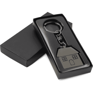 A gunmetal keychain in the shape of a house, elegantly packaged in a black box.