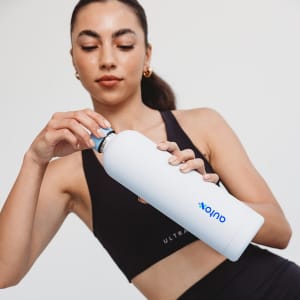 A drink bottle in white being held by a woman. The bottle features a logo and has a sleek design.