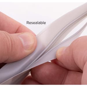 A hands holding a clear, resealable PEVA reusable food storage bag, showcasing its seal and material texture.