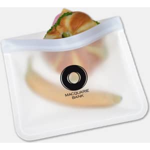 A clear PEVA reusable food storage bag containing a sandwich and a banana, featuring a logo.