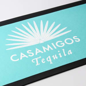 A turquoise bar runner featuring a palm leaf design and a logo, set against a black trim.