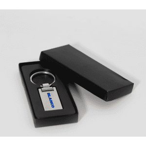 A silver keychain in a black presentation box, featuring a simple design and a logo.