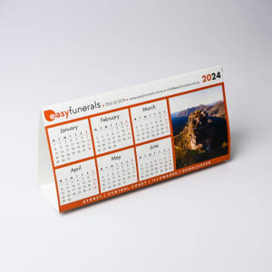 A desk calendar featuring a white and orange design with months displayed from January to June, including a scenic image.