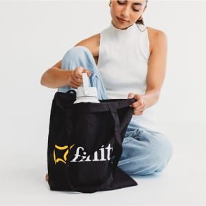 A black tote bag with a logo, being held by a person, while they reach inside for a drink bottle.