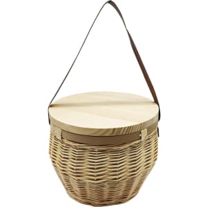 A natural woven basket with a round wooden lid and a brown shoulder strap. It features a textured finish.