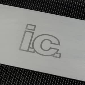 A stainless steel grilling spatula with engraved lettering on a textured black background.