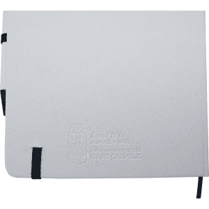 A white A5 notebook with a black elastic band and a black pen, featuring a subtle embossed logo.