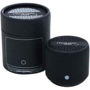 A black Bluetooth speaker with a textured top, placed next to a cylindrical box featuring a logo.