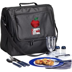 A black picnic basket set includes utensils, a drink glass, condiment containers, and a blue plate with food.
